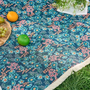 Detail of floral picnic mat with daisy patterns and white decorative fringes on grass