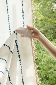 Detail of beige polyester curtain with blue geometric embroidery and fringe edges