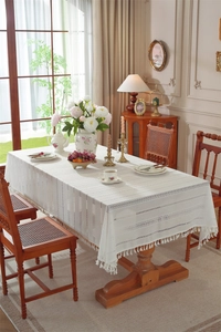 Detailed view of cream lace tablecloth with hollow stripes and tassel trim on wooden table