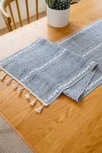 Macro view of blue jacquard table runner with white embroidery and cotton tassels