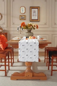Macro shot of white plush Halloween table runner with black ghost embroidery on wood table
