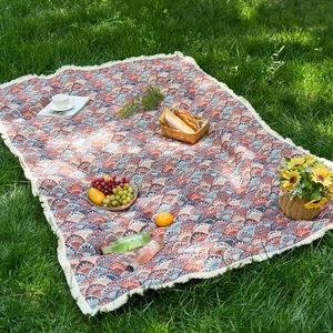 Outdoor jacquard picnic blanket with tassel edges on green grass with picnic basket