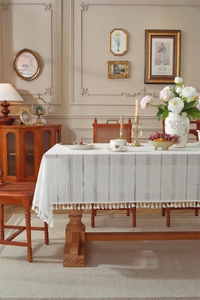 Close-up of French white lace tablecloth with hollow stripes and fringe on wooden table