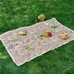 Outdoor vintage floral picnic mat with white tassels on green grass with picnic setup