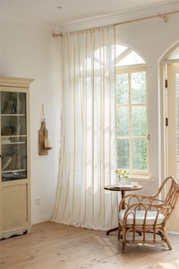 Detail of white polyester curtain with yellow stripes and elegant tassel fringe hanging