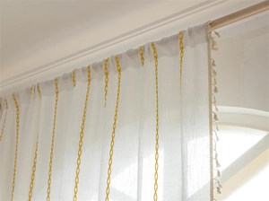 Detail of white jacquard curtain with yellow geometric diamond pattern and tassel trim