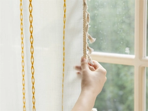 Detail of white semi-transparent curtain with yellow geometric embroidery and cream tassels