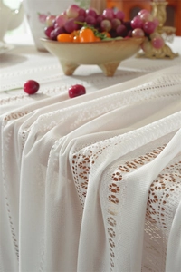 Detail of white hollow lace tablecloth with elegant stripe pattern and fringe texture
