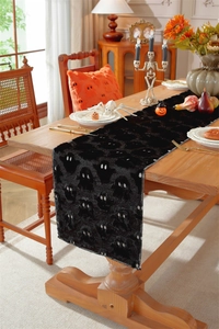 Detail of black plush Halloween table runner with white ghost embroidery on wooden table
