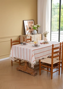 Detailed view of beige polyester tablecloth with orange stripes and fringe tassels