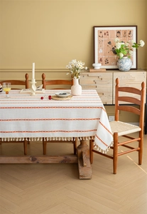 Detailed view of white polyester tablecloth with orange embroidery and fringe trim