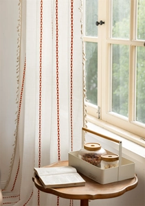 Detail of bohemian cream curtain featuring red geometric diamonds and white tassel trim