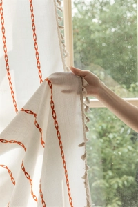 Detail of white curtain with orange geometric embroidery and delicate fringe trim