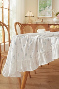 Detail of white floral tablecloth with blue leaf print and ruffled hem on wooden table