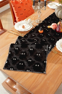 Close-up of black plush Halloween table runner with white embroidered ghost eyes detail