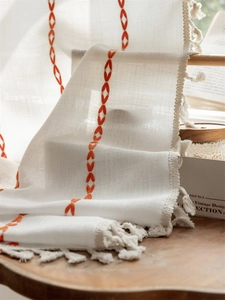 Detailed close-up of geometric embroidery and beige tassels on bohemian curtain fabric