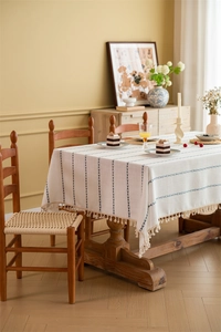 Macro detail of beige jacquard tablecloth featuring blue geometric embroidery and fringe