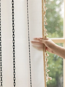 Detail showing hand touching boho curtain with black embroidery and beige tassel edges