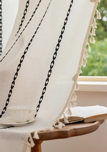 Close-up of geometric pattern and fringe tassels on bohemian cream window curtain