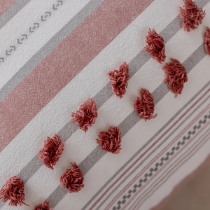 Macro detail of Nordic textured pillowcase with terracotta tufted tassels and woven stripes