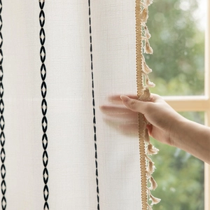 Detail of geometric diamond embroidery and cotton tassel trim on boho linen curtain