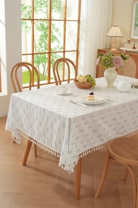Detail of white cotton tablecloth with blue botanical print and white tassel ball trim
