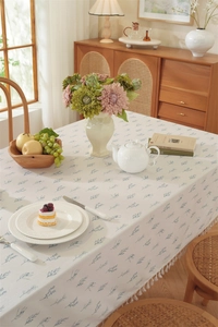 Detail of cotton tablecloth with blue leaf print and white tassel edge on wood table