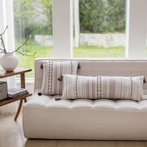 Detail of pink and gray striped pillow covers with pom-poms and tassels on a sofa