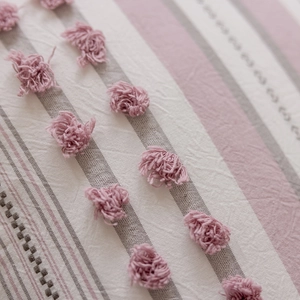 Detail of pink pompoms and textured striped fabric on a Nordic style cushion cover