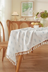Close-up of cotton floral tablecloth featuring blue leaf prints and white tassel edges