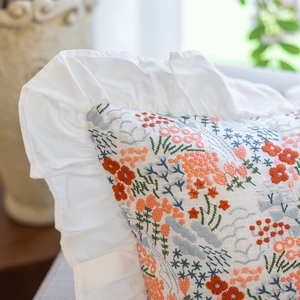 Detail of colorful floral embroidery on white cotton pillowcase with ruffle edges