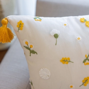 Close-up of floral embroidery detail and yellow tassel fringe on cotton cushion cover