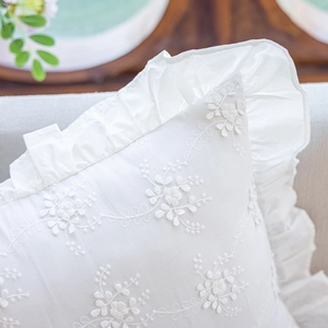 Close-up of white cotton cushion cover with floral embroidery and ruffle trim details