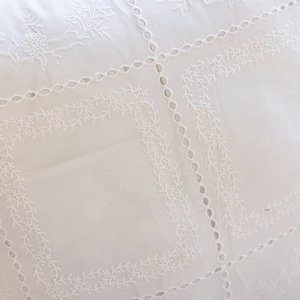Detailed close-up of white cotton embroidery with floral ruffles and eyelet lace fabric
