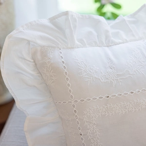 Close-up of white cotton pillowcase with floral embroidery and ruffle trim detail