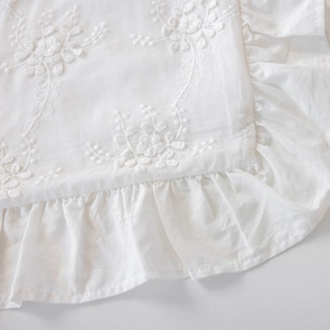 Close-up of white cotton pillowcase featuring floral embroidery and ruffled edges