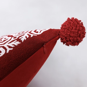 Dettaglio del copricuscino natalizio rosso con jacquard a fiocco e pompon morbido