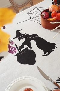 Detail of Halloween tablecloth featuring black witch and spider web on white fabric