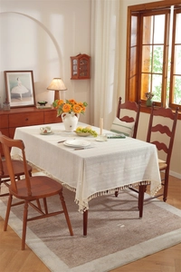 Detail of cream linen-textured tablecloth featuring decorative fringe tassels on table