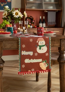 Detail of red Christmas table runner with snowman patterns and red pom-pom trim on wood table