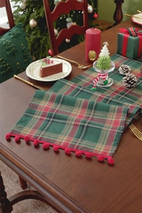 Detailed texture of red and green plaid Christmas table runner with festive pom-pom trim