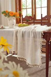 Detail of cream linen tablecloth featuring vertical stripes and elegant fringe tassels
