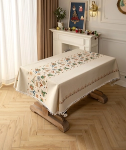 Detailed view of beige Christmas tablecloth with reindeer prints and white pom-pom trim