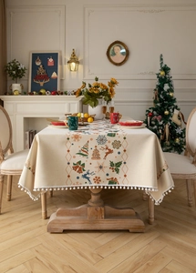 Detailed view of beige Christmas tablecloth with reindeer patterns and white pom pom fringe