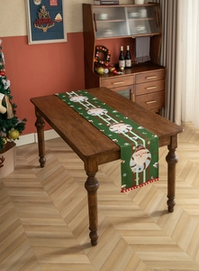 Close-up of green Christmas table runner with Santa patterns and red pompom fringe trim