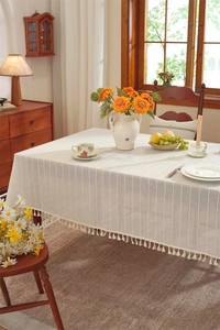 Close-up of cream linen tablecloth featuring vertical stripes and elegant fringe tassels