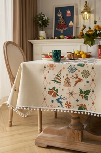 Detailed view of Christmas tablecloth featuring colorful reindeer and white pompom fringe