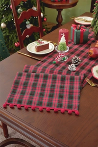 Detail of Christmas table runner with red and green plaid pattern and festive pom-poms