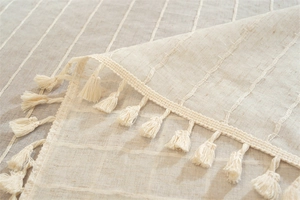 Detail shot of beige linen tablecloth with vertical stripes texture and fringe tassel edge