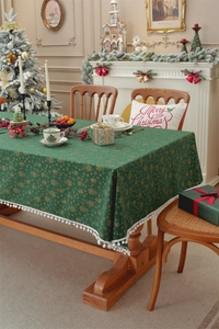 Close-up of green Christmas tablecloth with gold bell patterns and white pompom fringe
